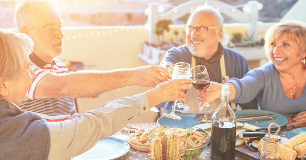 seniors are enjoying their food and drink in restaurant, cheers with red wine.