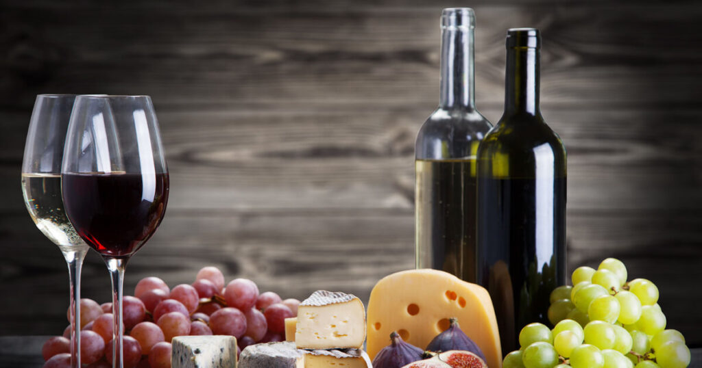 Italian wine bottles, a bunch of grapes, two glasses of wine, cheese.