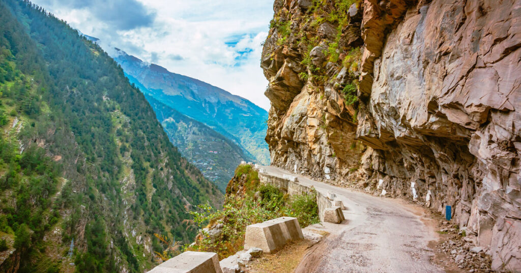 a narrow road in India, mountains around, road near big rocks.